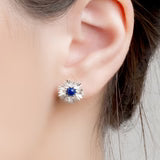 Close-up of a lapis lazuli and silver flower earring with a blue gemstone worn by a person.