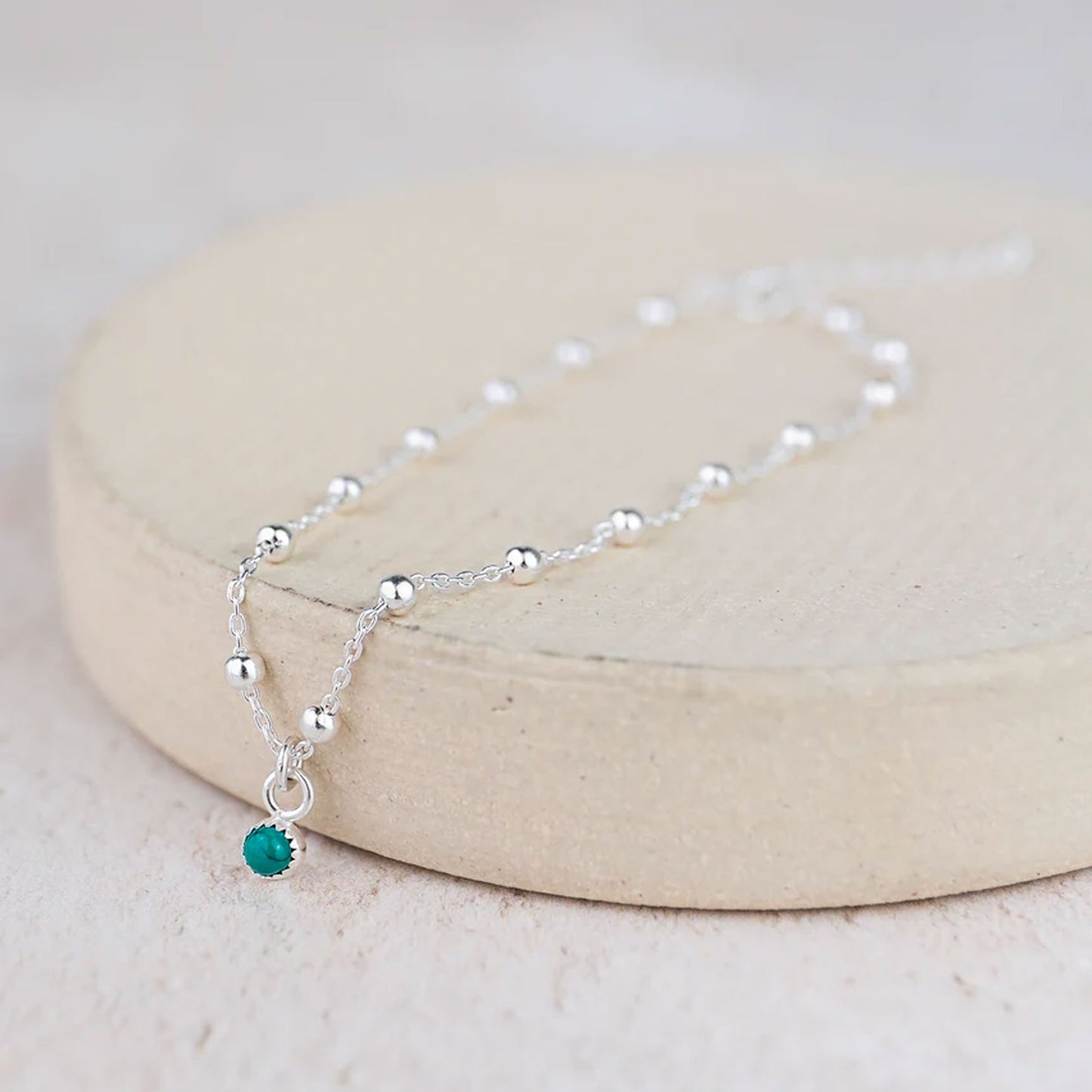 Silver necklace with a green bead on a beige stand