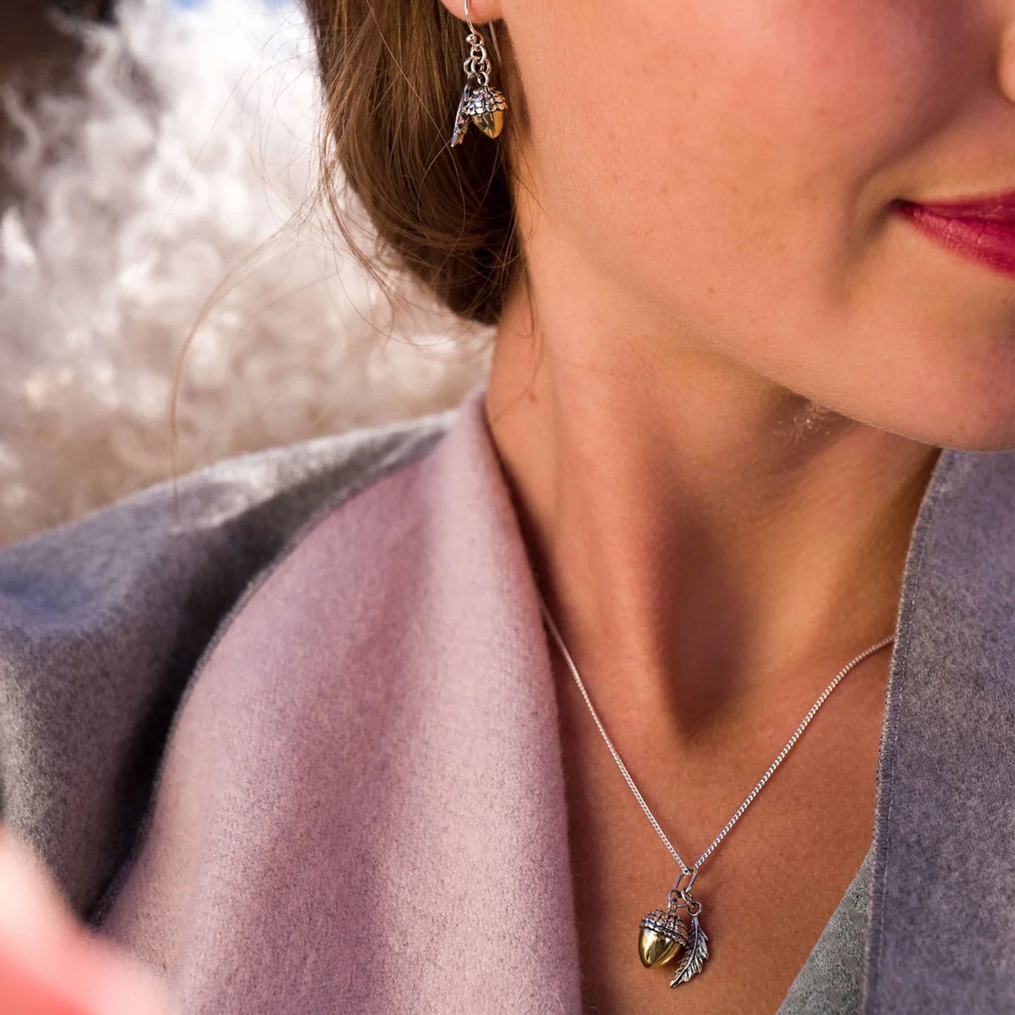 Close-up of a woman wearing a silver acorn necklace with a pendant, blurred background