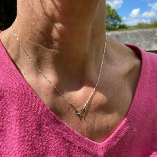 Person wearing a pink shirt with a necklace featuring a green leaf pendant outdoors.