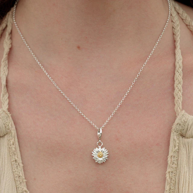 Silver necklace with a daisy pendant on a person wearing a beige top.