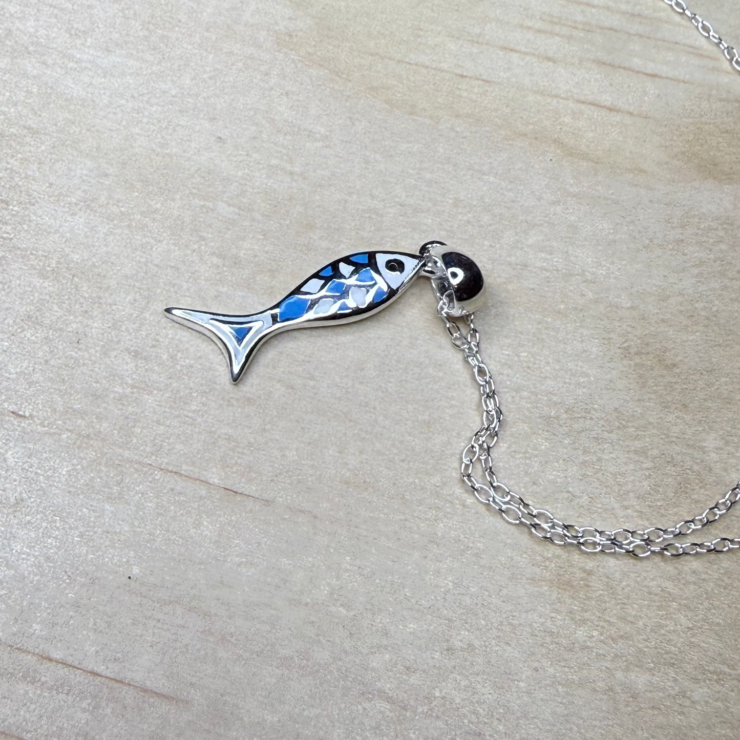 Fish-shaped pendant on a chain against a light wood background