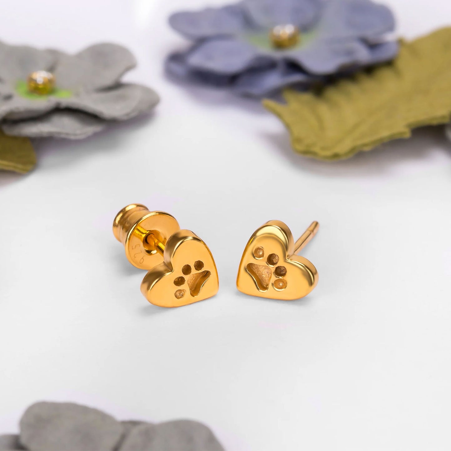 Gold heart-shaped earrings on a white background with flowers.