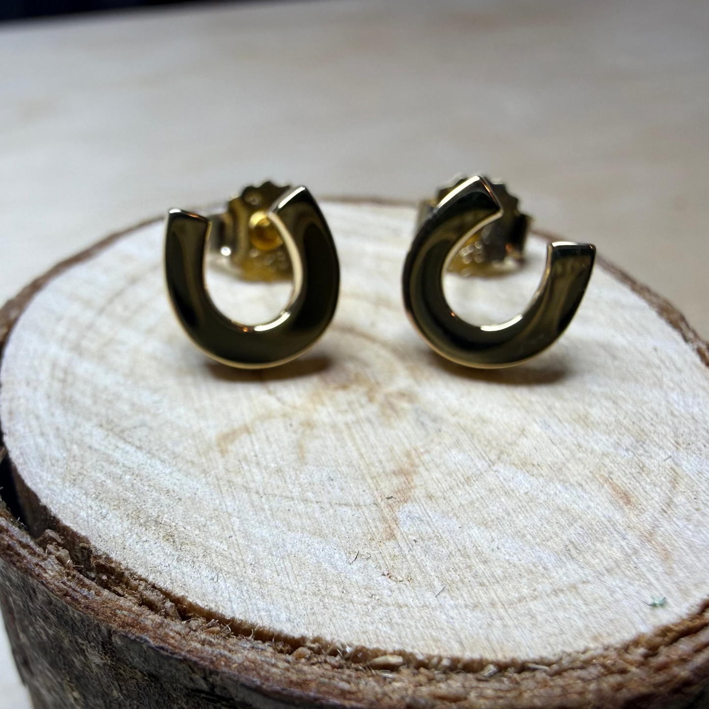 Gold horse shoe earrings on a white wood surface