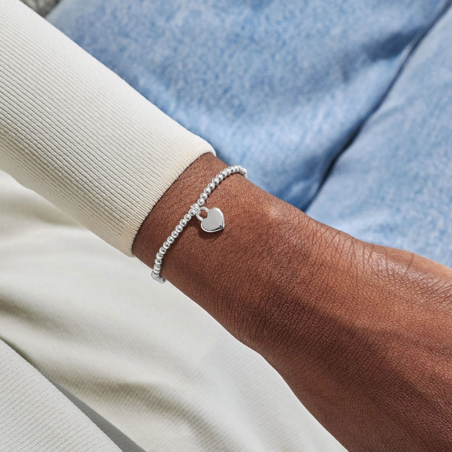 Silver bracelet with a heart charm on a wrist against a blue denim background