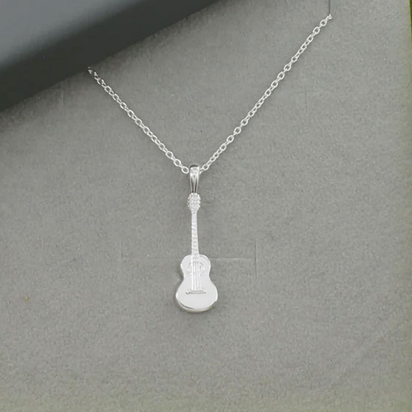Silver guitar-shaped pendant on a chain against a gray background