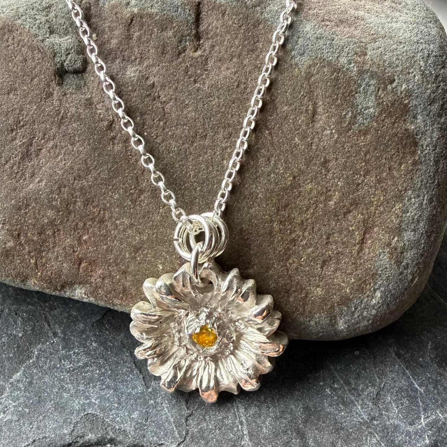 Silver necklace with a sunflower pendant on a stone surface