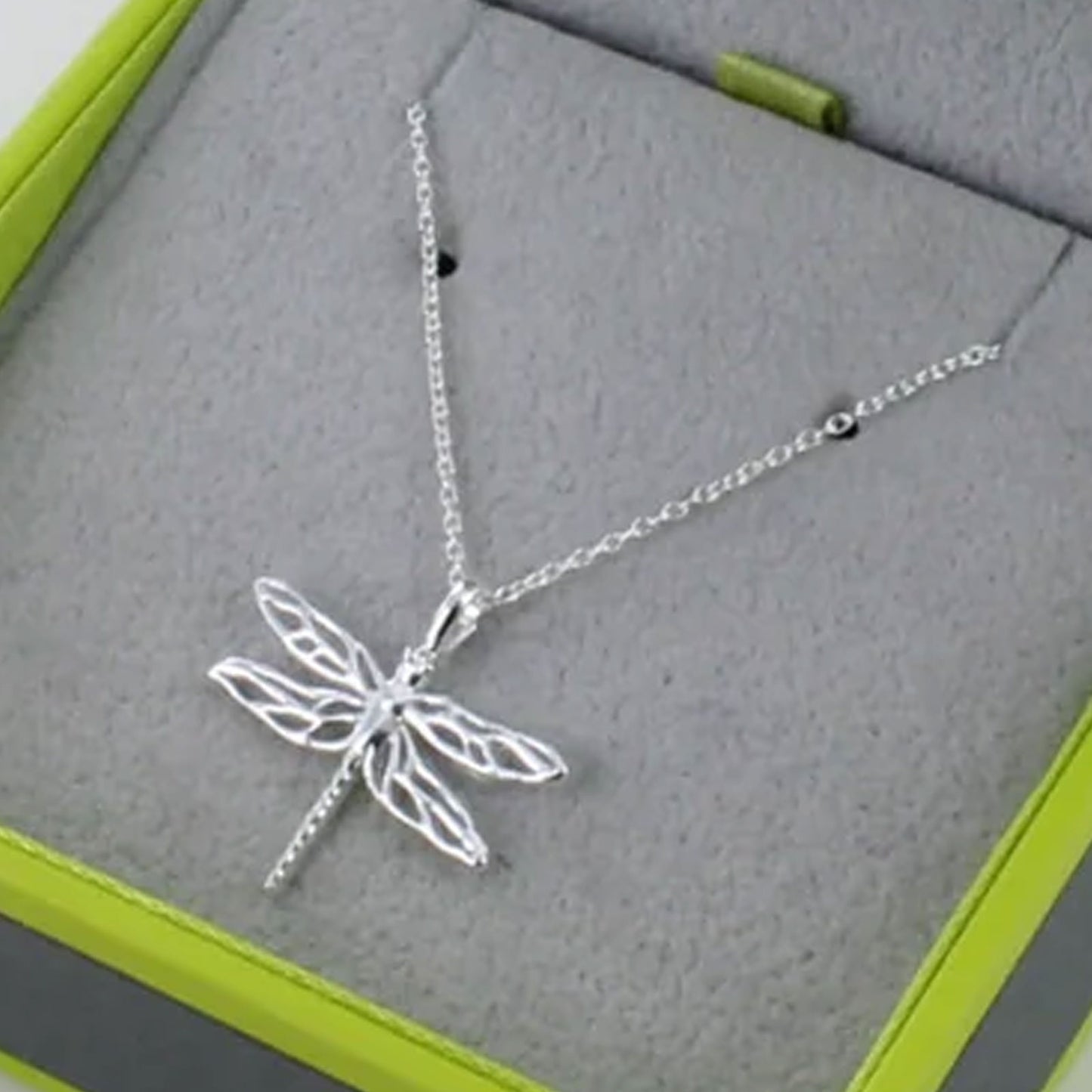 Silver dragonfly necklace on a gray surface with green edges