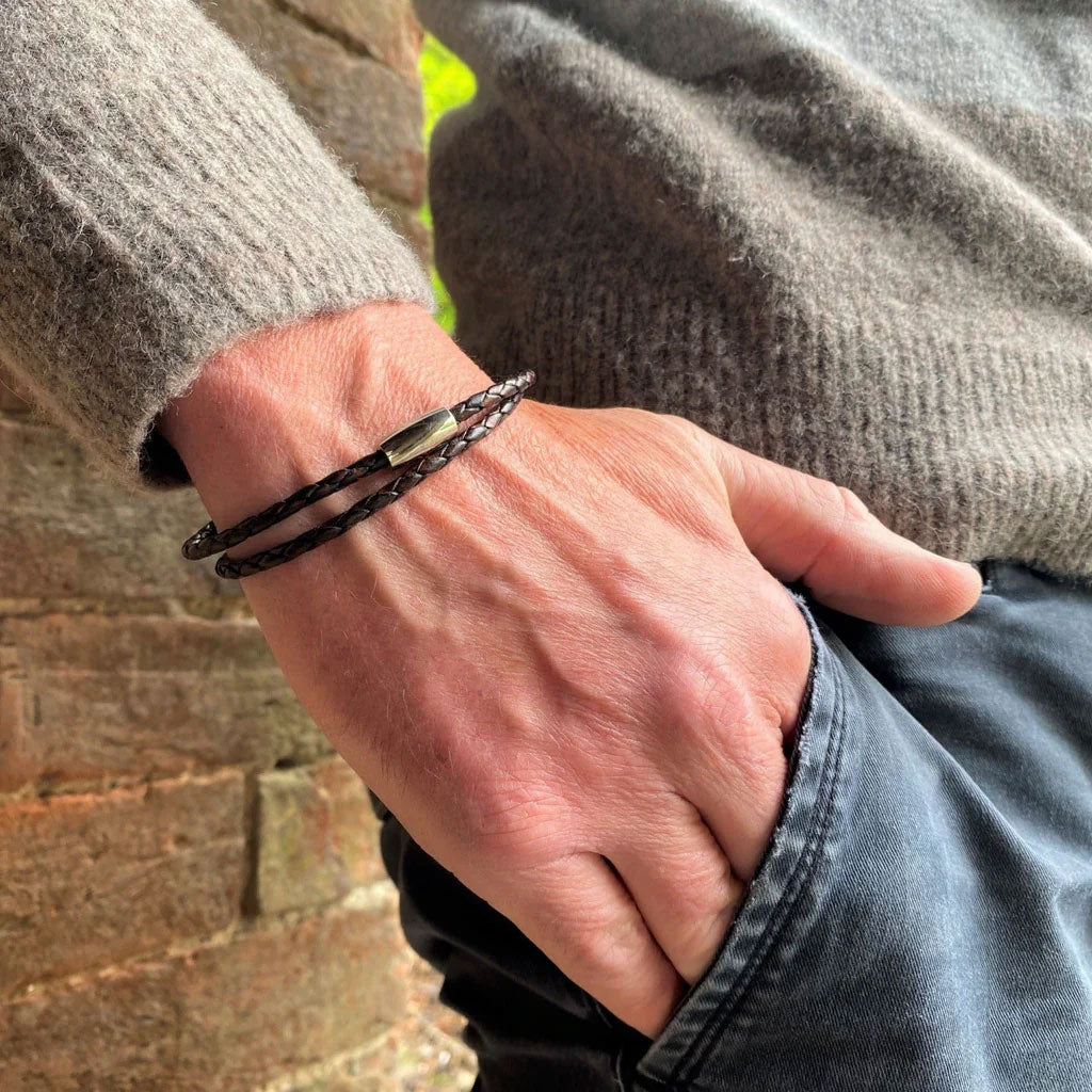 Hand wearing a bracelet with a clasp, against a blurred brick wall background