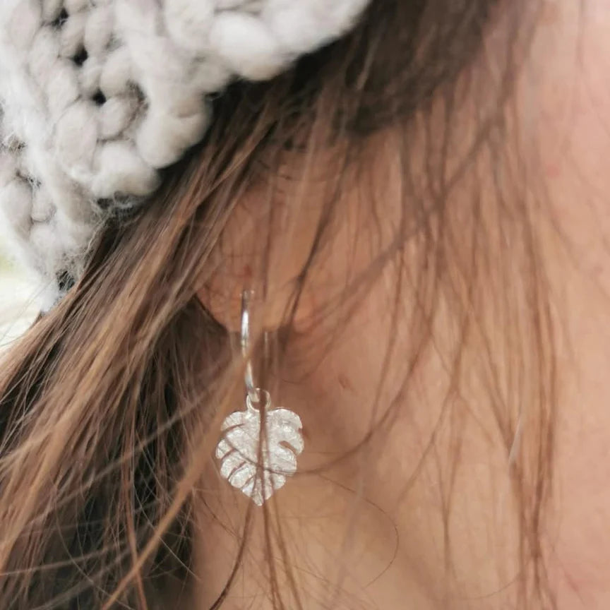 Close-up of a person wearing silver leaf earrings with a blurred background