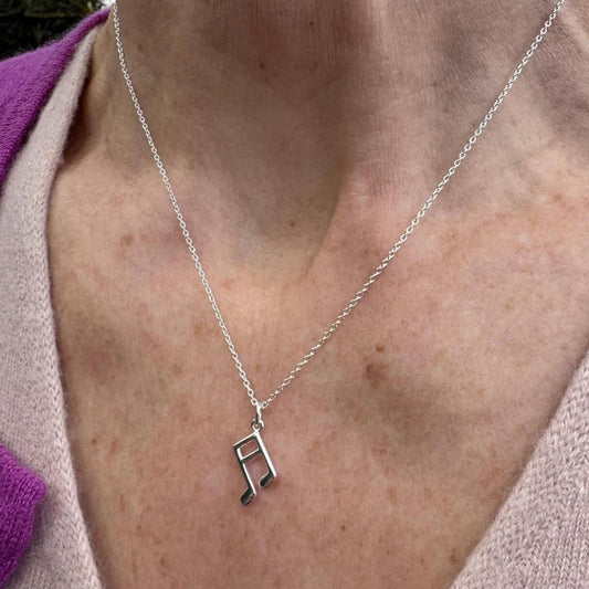Silver necklace with a music note pendant on a person's neck