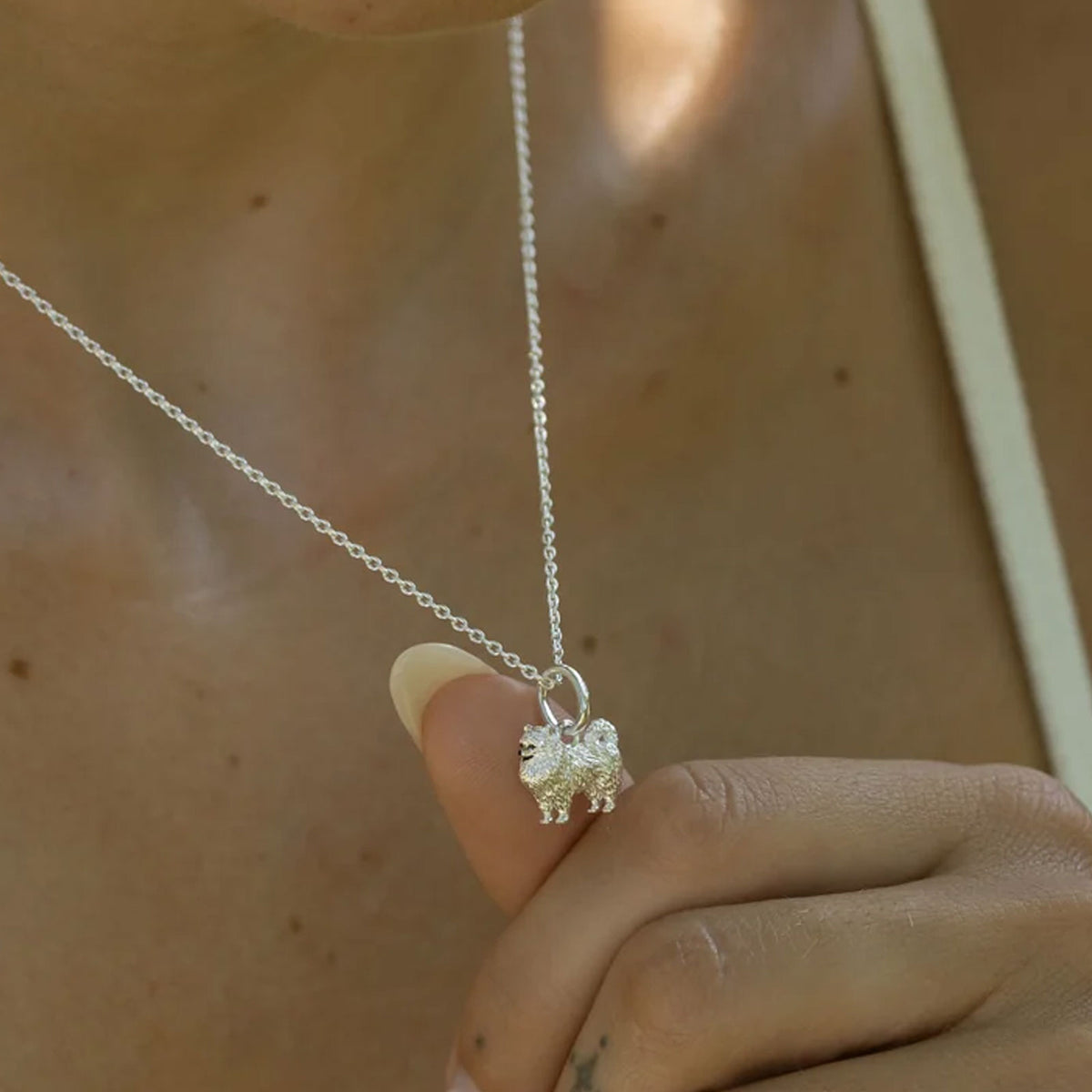 Silver dog necklace with a small pendant held by a hand against a neutral background