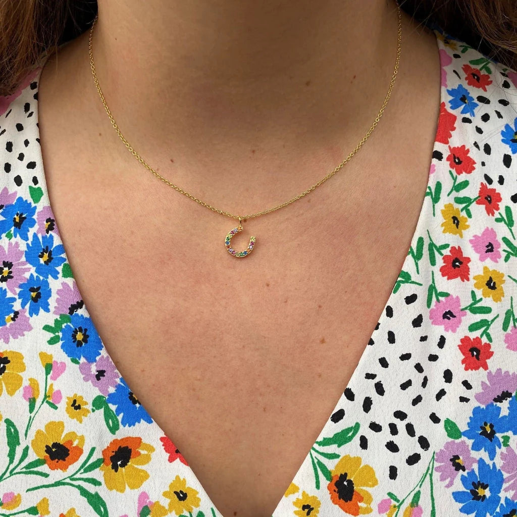 Gold necklace with a small pendant worn by a person against a floral background