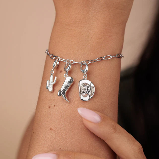 Silver bracelet with cactus, boot, and rose charms on a wrist against a neutral background