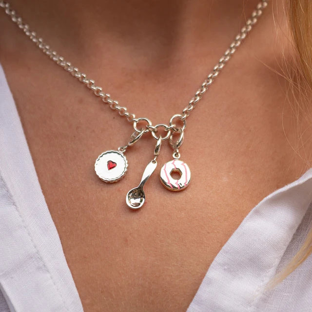 Necklace with charms featuring a heart, spoon, and donut on a person wearing a white shirt.