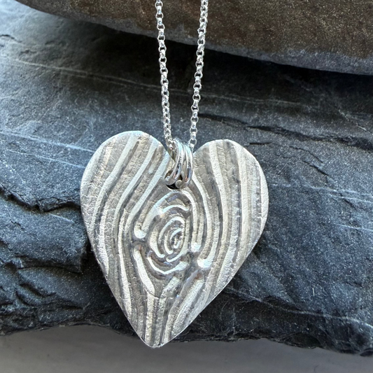Silver heart-shaped pendant on a chain against a stone background