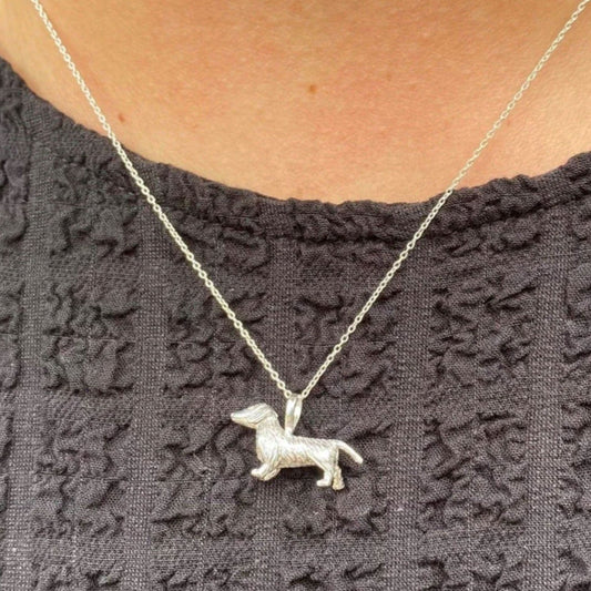 Silver dog-shaped pendant necklace on a person wearing a dark textured top.