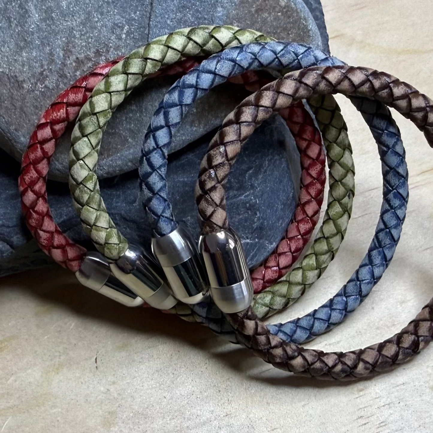 Set of braided leather bracelets in various colors on a stone surface
