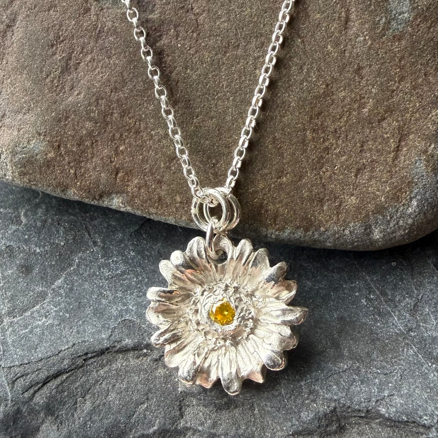 Silver necklace with a flower pendant on a stone surface