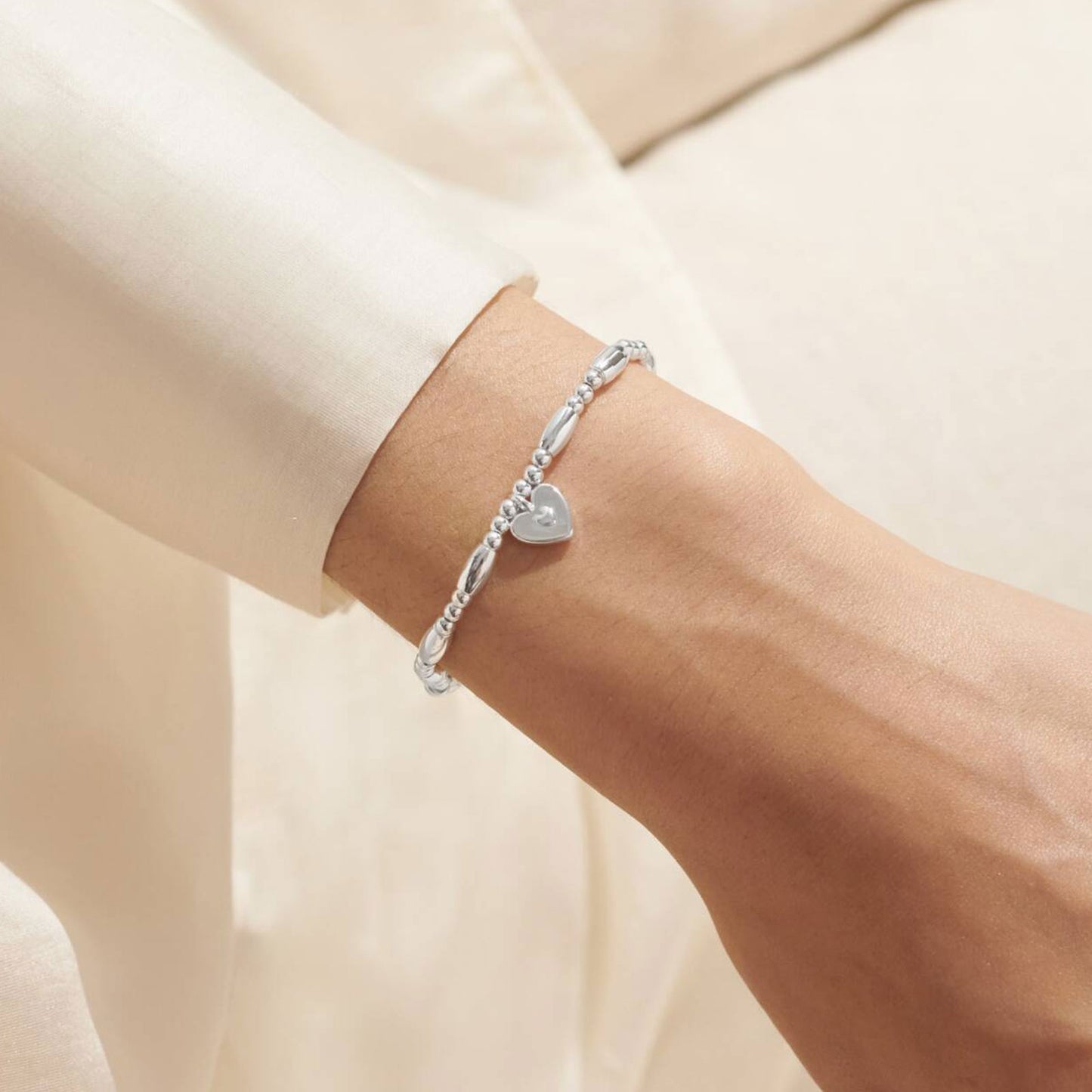 Silver bracelet with a heart charm on a wrist against a neutral background