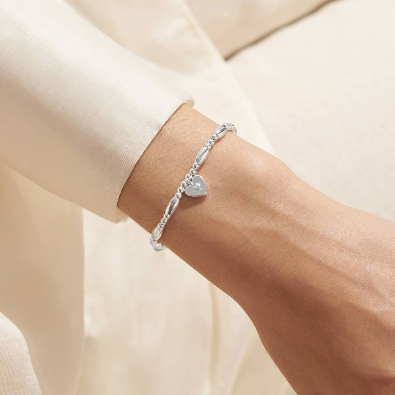 Silver bracelet with a heart charm on a wrist against a neutral background