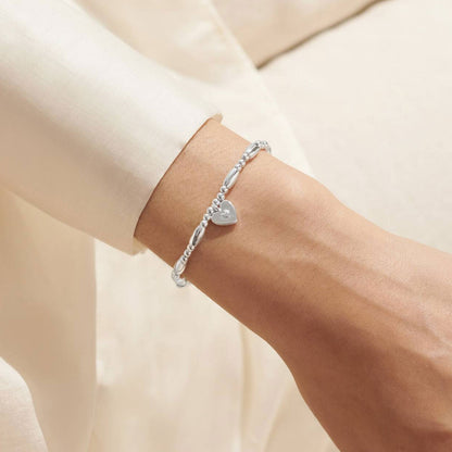 Silver bracelet with a heart charm on a wrist against a neutral background