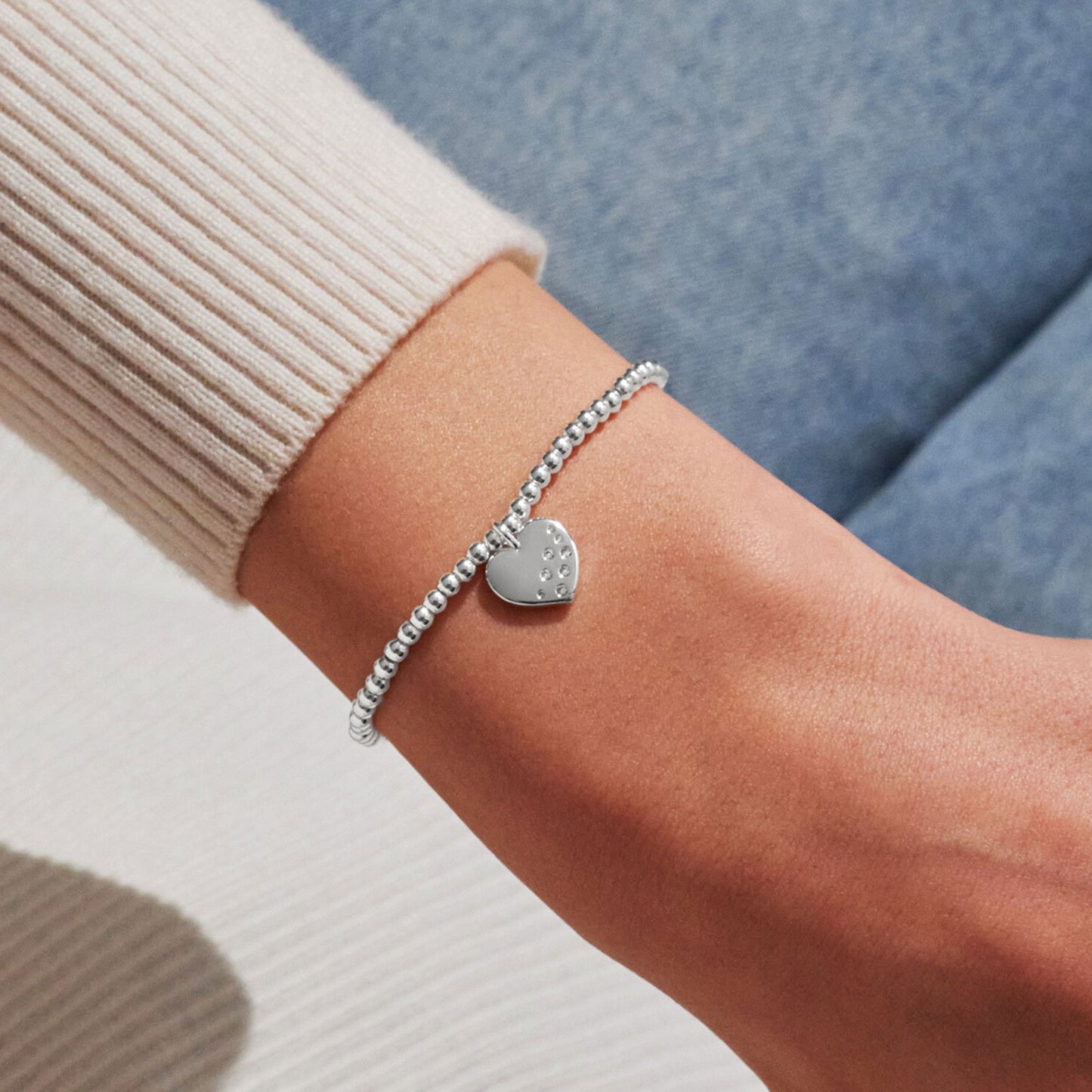 Silver bracelet with a heart-shaped charm on a wrist against a neutral background