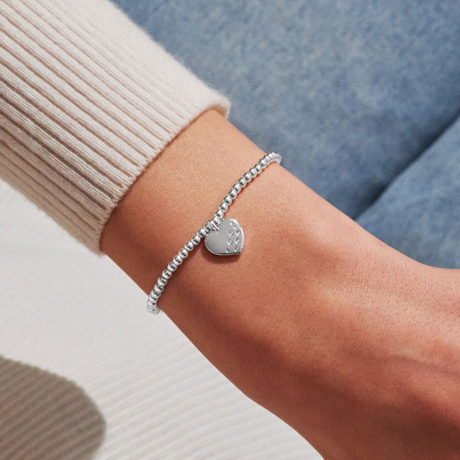 Silver bracelet with a heart-shaped charm on a wrist against a neutral background