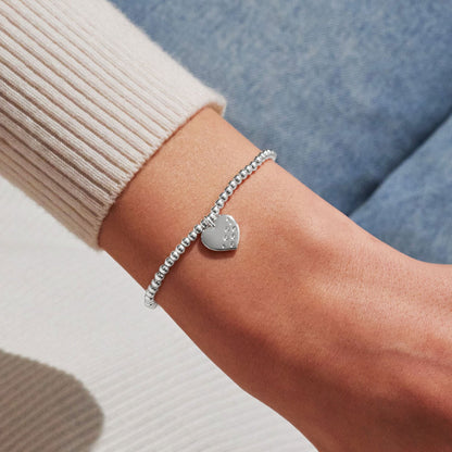 Silver bracelet with a heart-shaped charm on a wrist against a neutral background