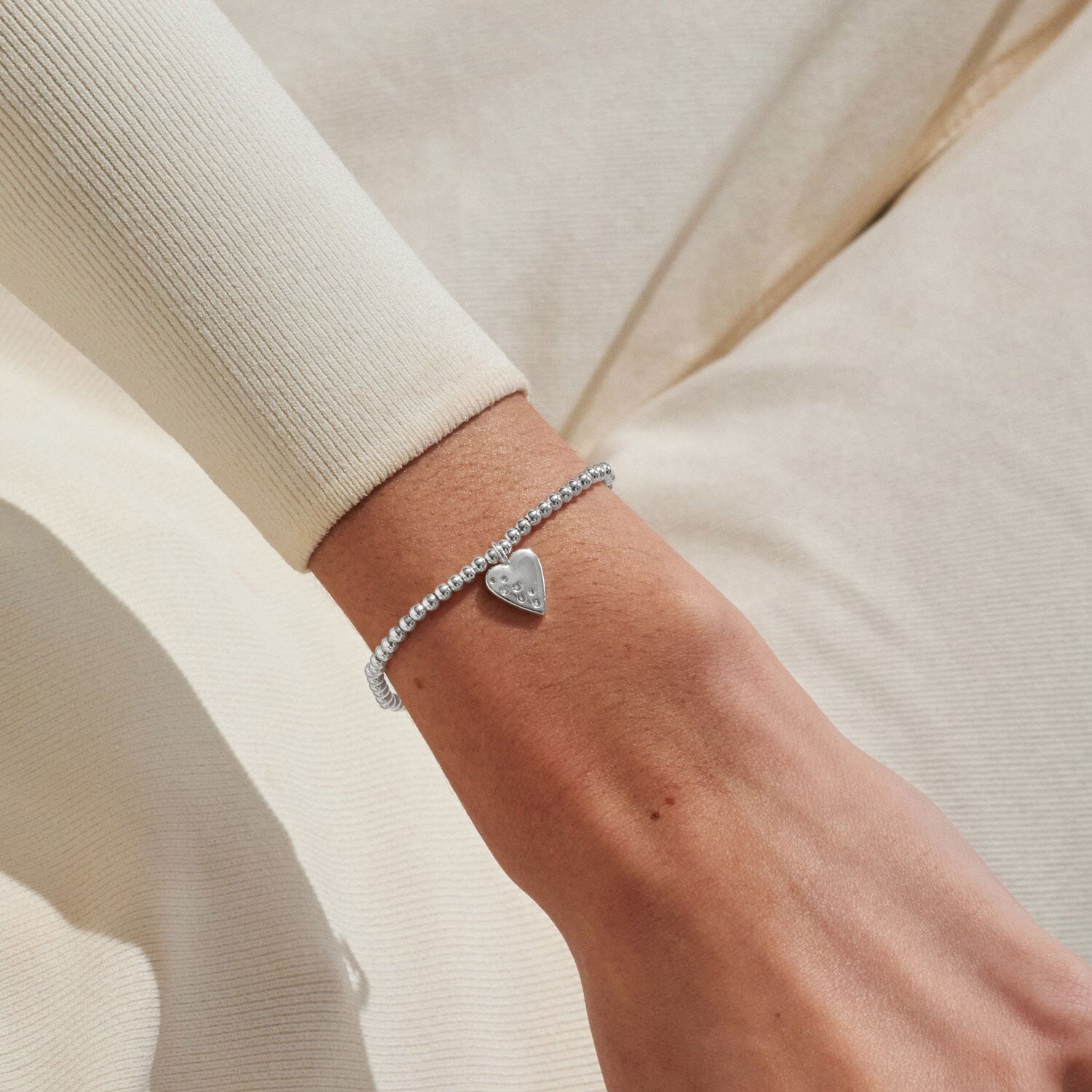 Silver heart bracelet on a wrist with a neutral background