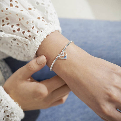 Close-up of a person's wrist wearing a silver bracelet with a heart charm.
