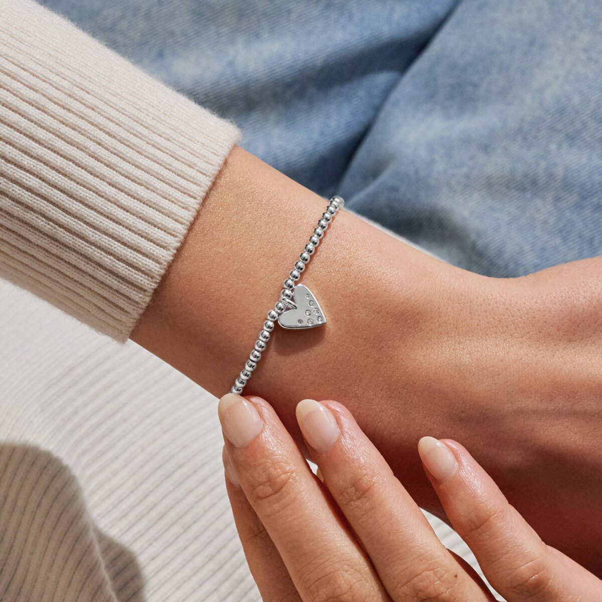Silver bracelet with a heart charm on a wrist against a neutral background