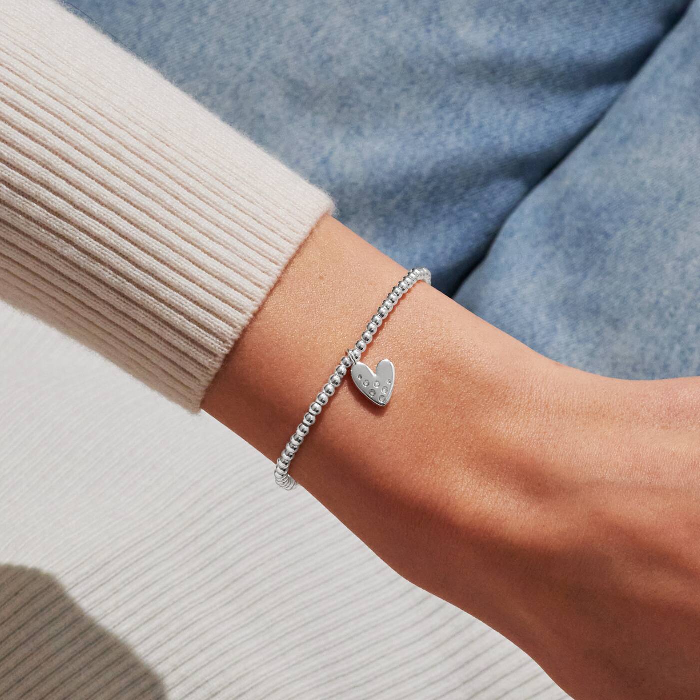 Silver heart bracelet on a wrist with a neutral background