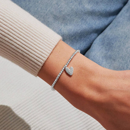 Silver heart bracelet on a wrist with a neutral background