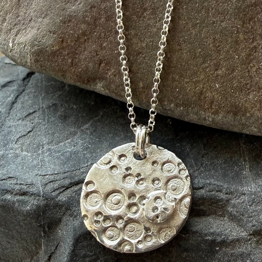 Silver necklace with a textured pendant on a stone surface