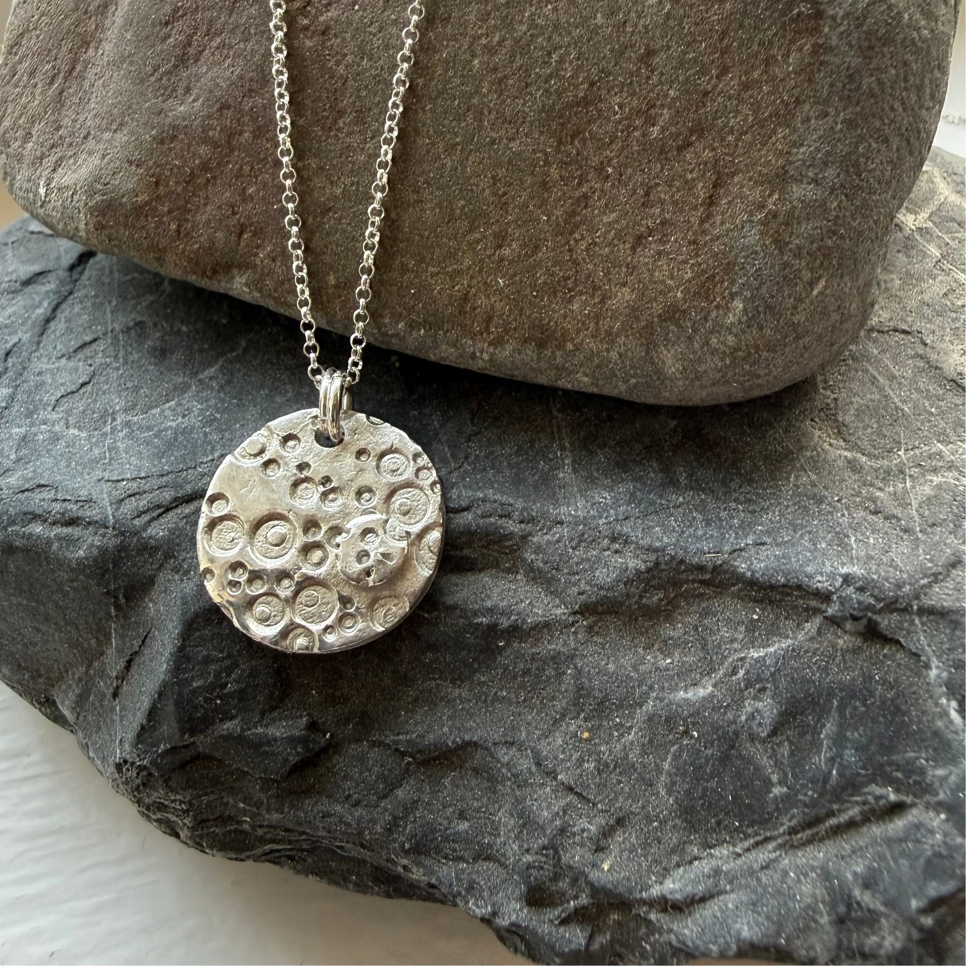 Silver necklace with a textured pendant on a stone surface
