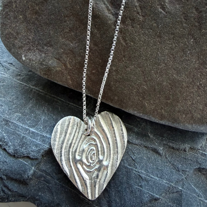 Silver heart-shaped pendant on a chain resting on a stone surface