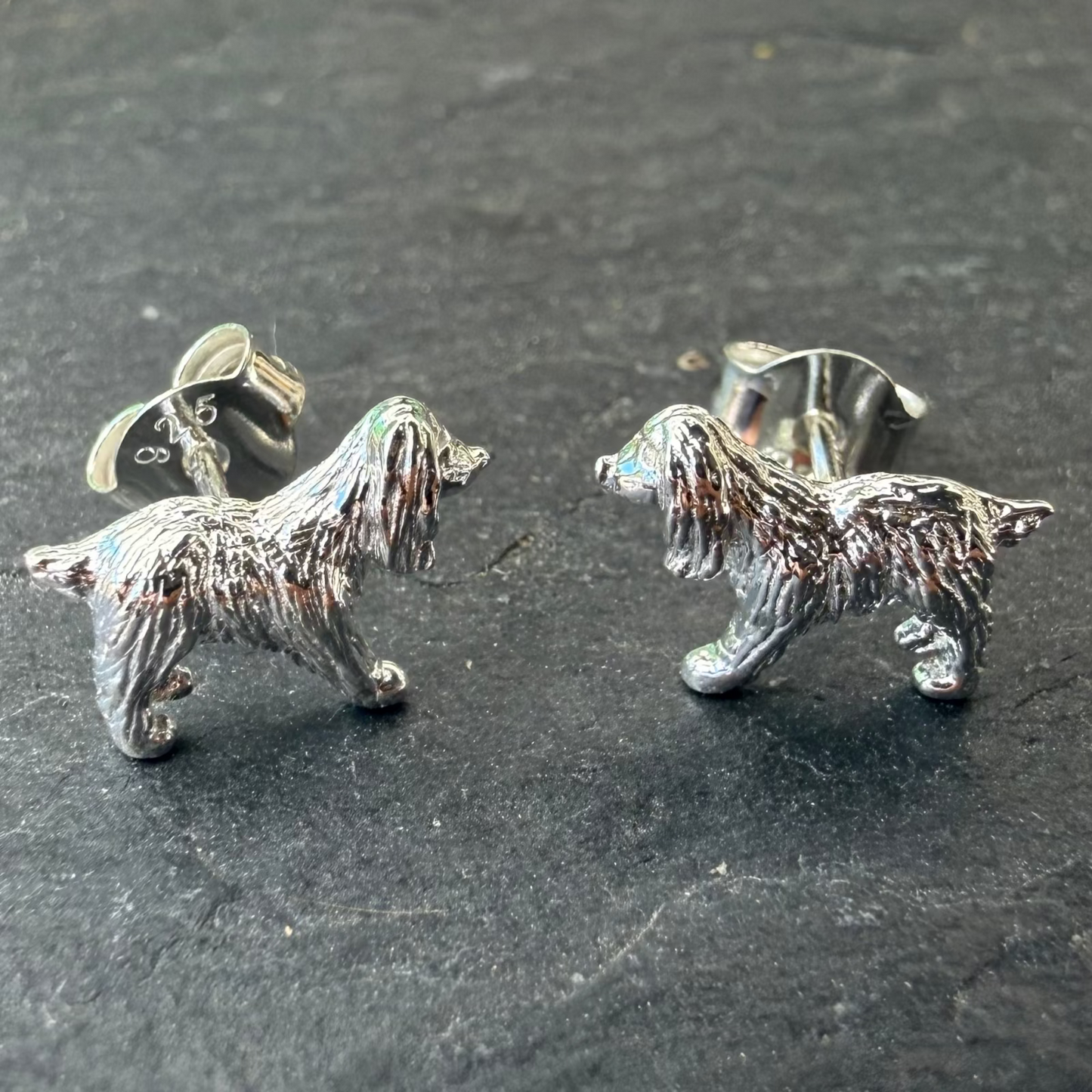 Silver spaniel dog-shaped earrings on a dark surface
