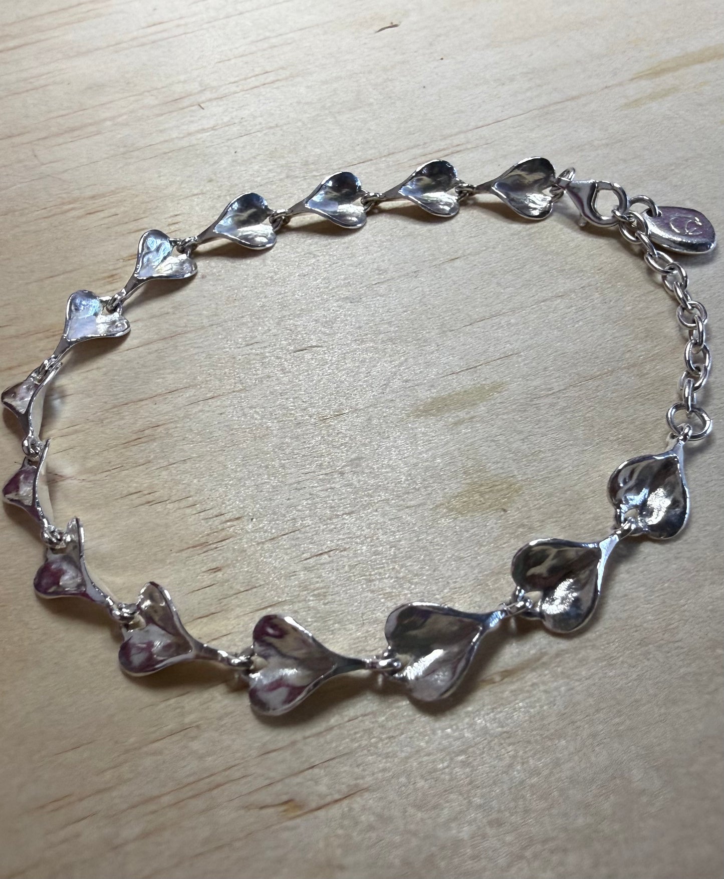 Silver bracelet with heart-shaped links on a wooden surface