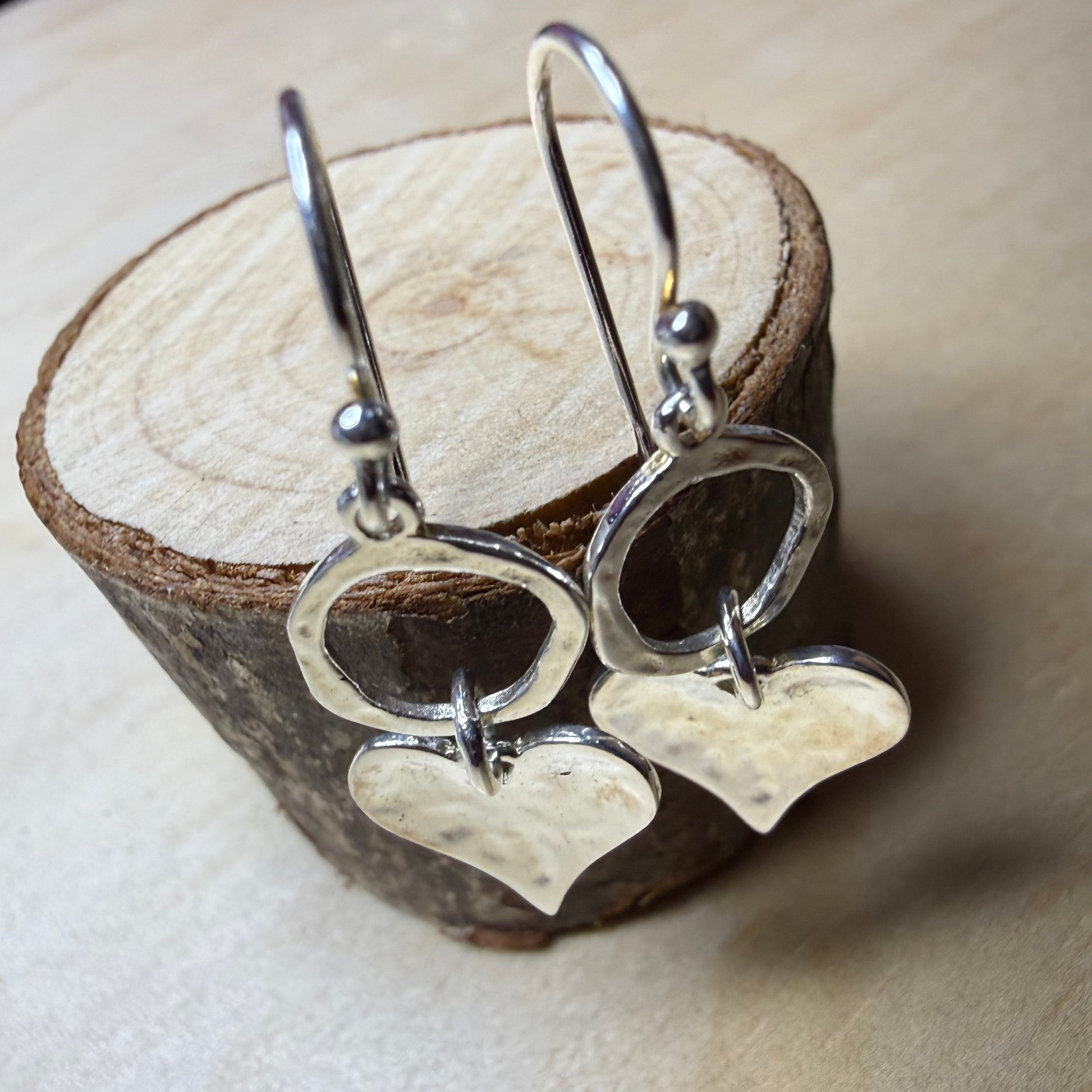 Silver heart-shaped earrings on a wooden stand.