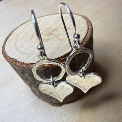 Silver heart-shaped earrings on a wooden stand.