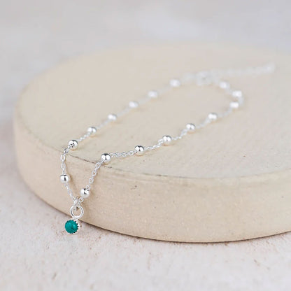 Silver necklace with a green bead on a beige stand