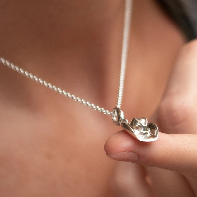 Silver necklace with a pendant held by a hand against a blurred background
