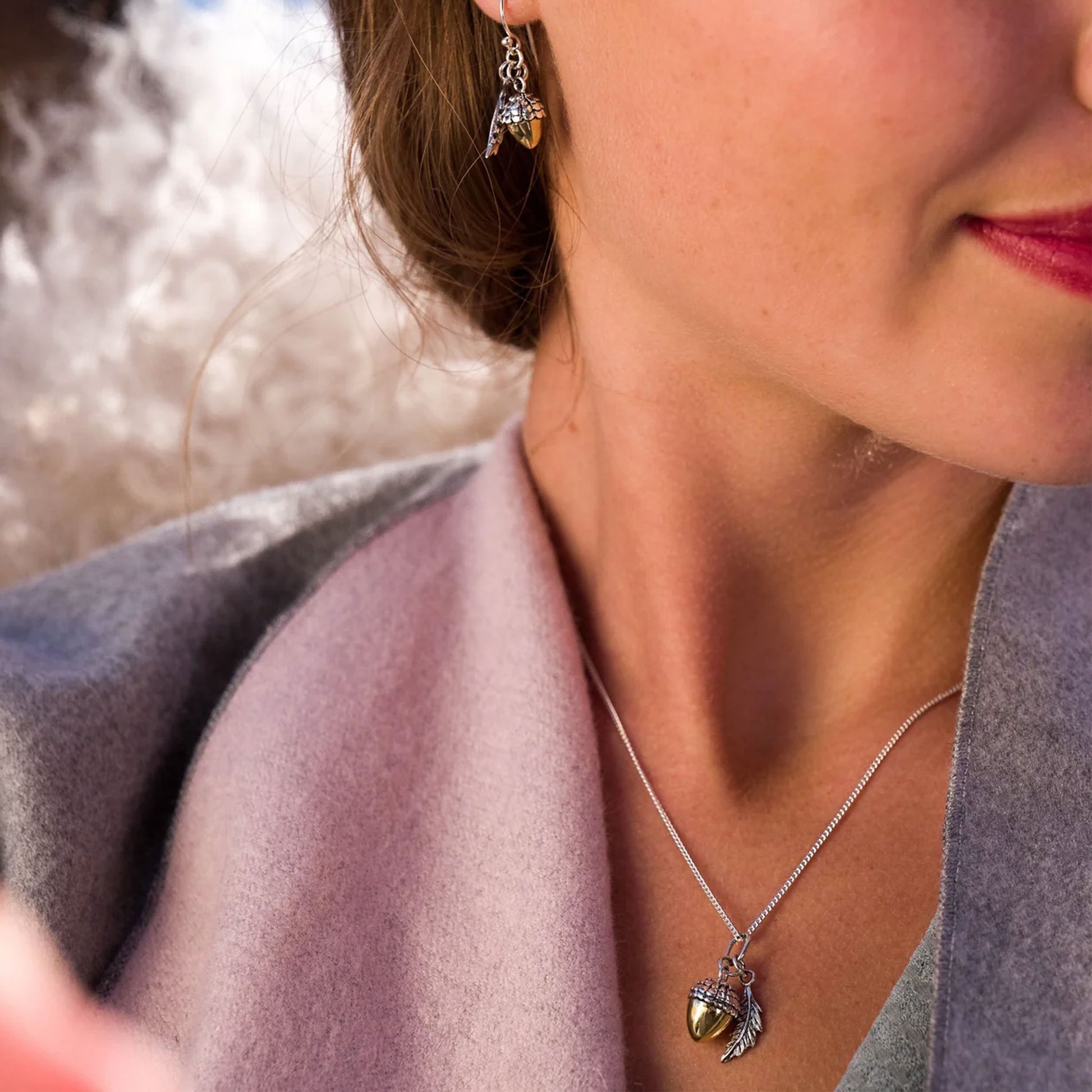 Close-up of a woman wearing a silver acorn necklace with a pendant, blurred background