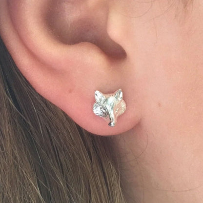 A close-up of a person's ear wearing a small silver stud earring shaped like a fox head.