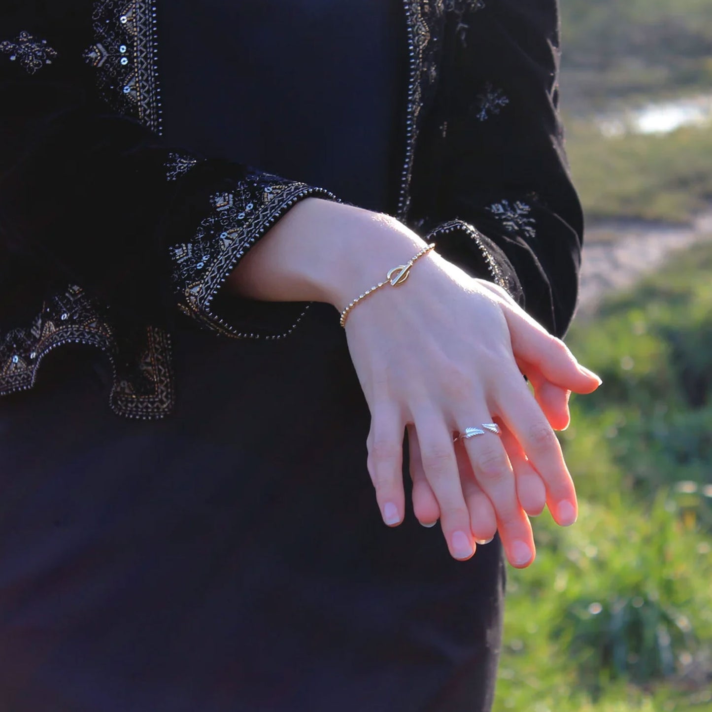 Person wearing a black jacket with floral patterns, holding hands with another person outdoors.