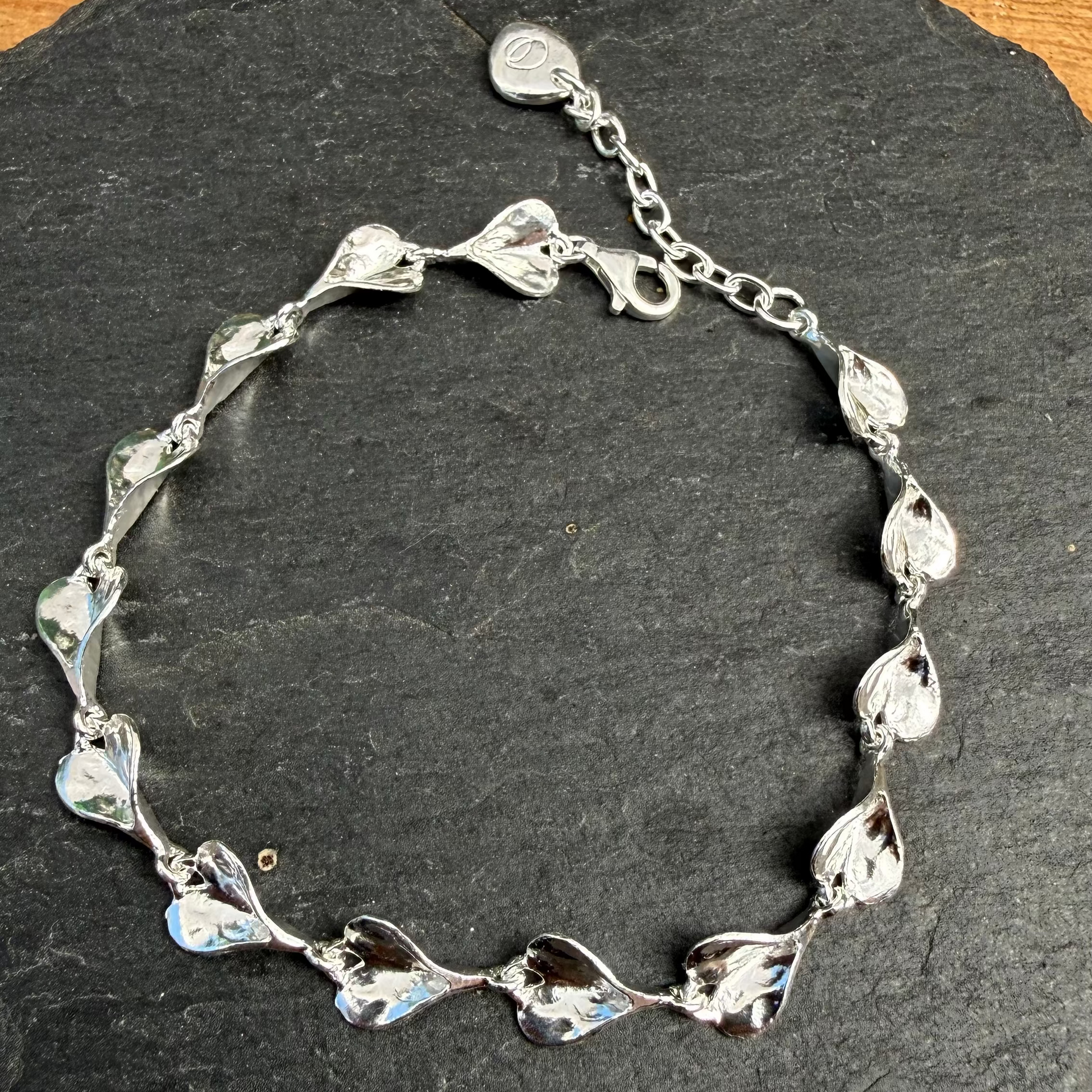 Silver hearts bracelet on a dark stone surface with a wooden background