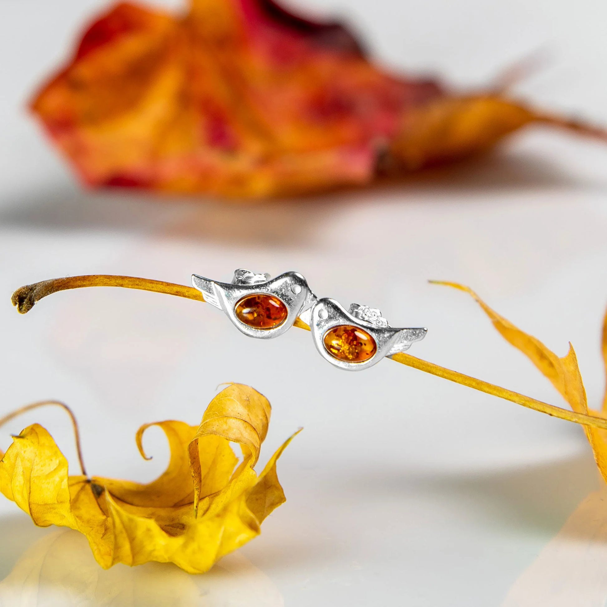Silver earrings with amber stones on a branch with autumn leaves