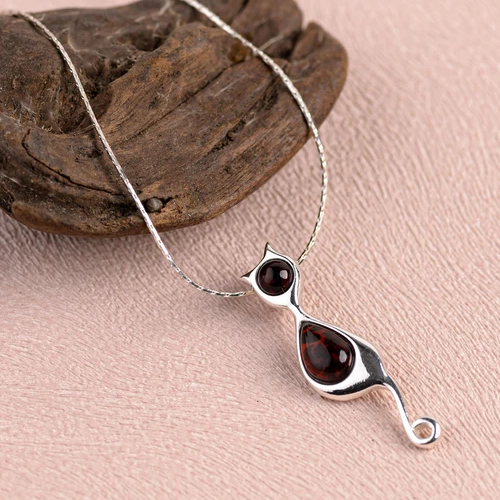 Silver necklace with a cat-shaped pendant featuring red stones on a pink surface.