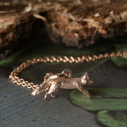 Rose gold fox-shaped pendant on a chain against a natural background